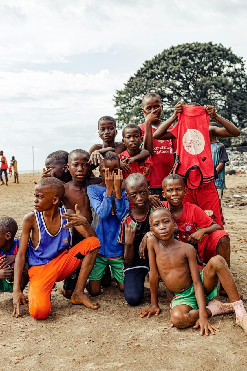 Children on a sandy shore, one holding up a red football jersey